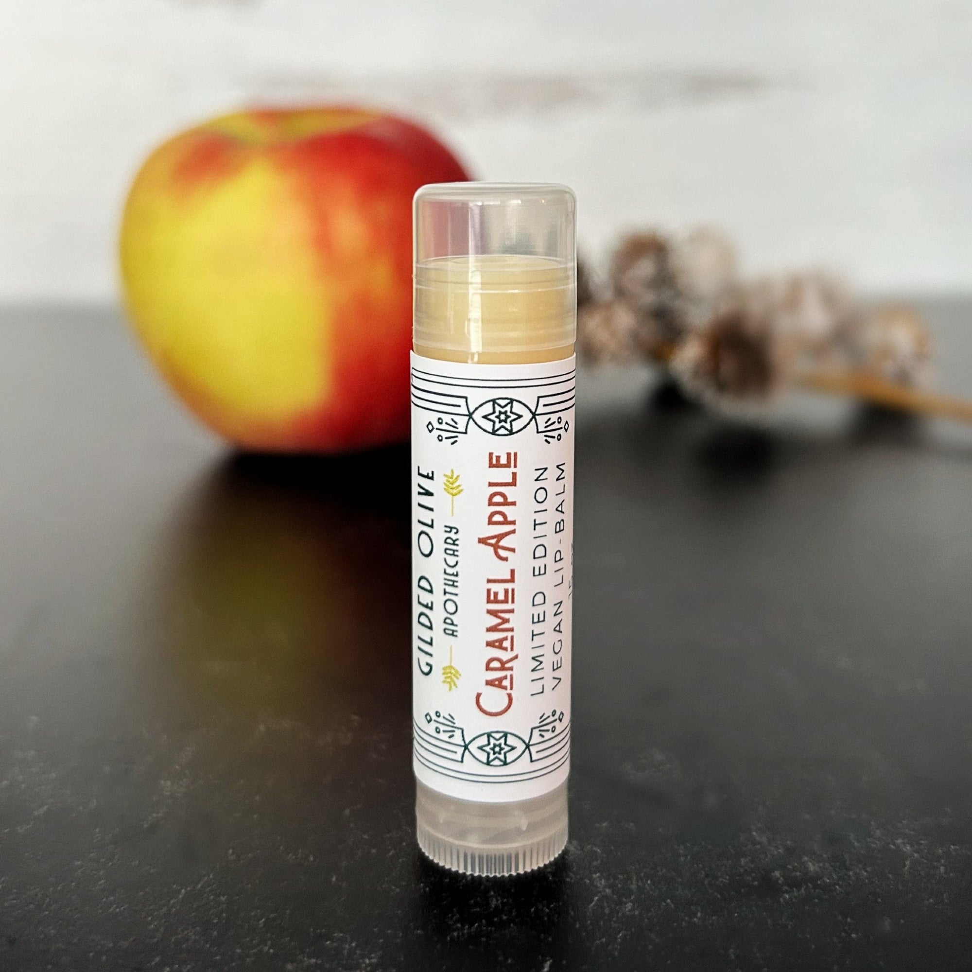 Caramel Apple Lip balm on a dark surface with an apple in the background