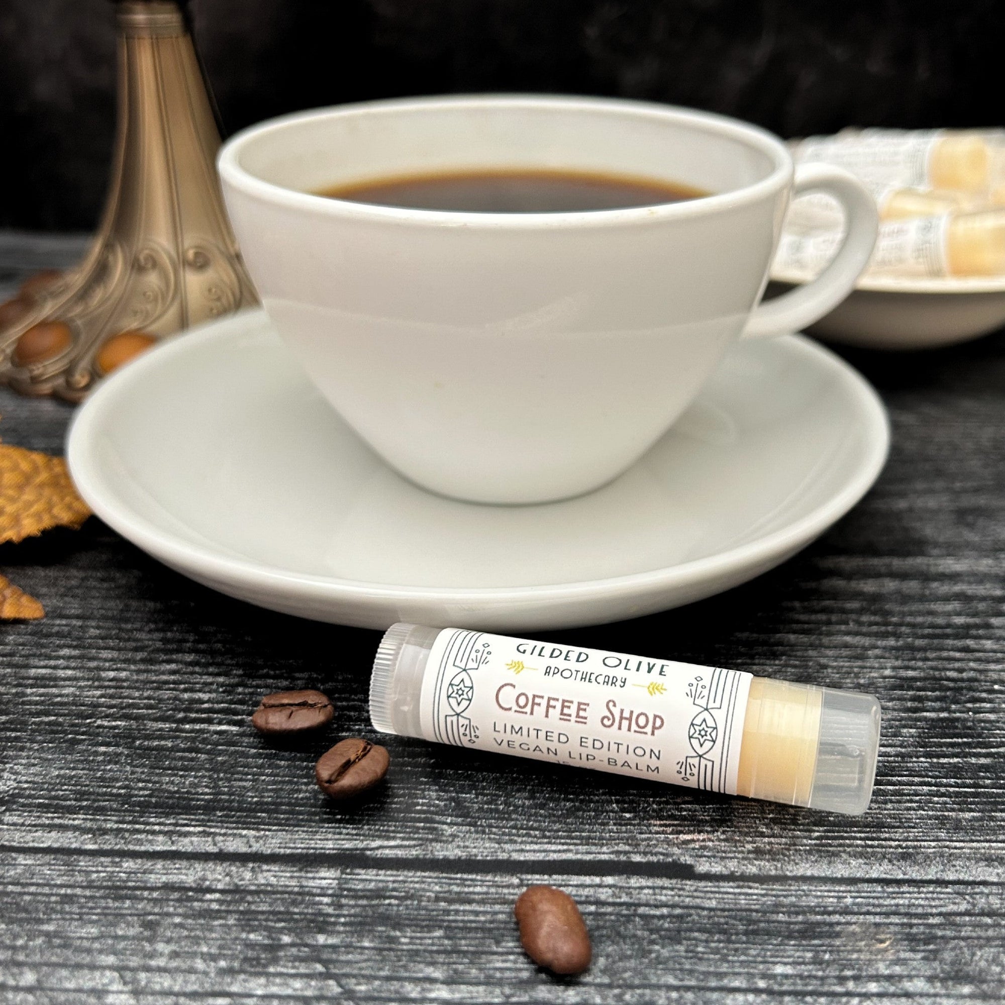 Coffee Shop Lip Balm next to a cup of coffee on a wooden surface with coffee beans