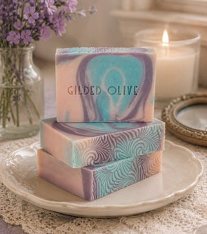 Golden Hour soap bars on a plate with purple flowers and a candle in the background