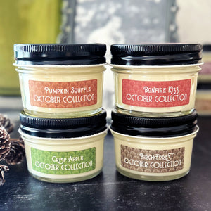 Four jars of 'The October Collection' 4 oz soy candles with colorful labels on a dark surface.