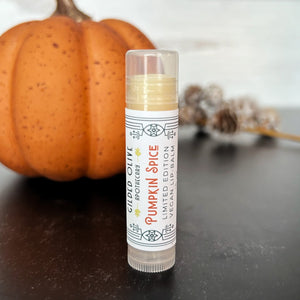 Pumpkin Spice Lip Balm in front of a pumpkin on a dark surface.