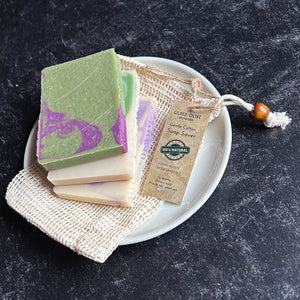 Three handmade soap bars on a white plate with a beige cotton drawstring pouch and hang-tag. 