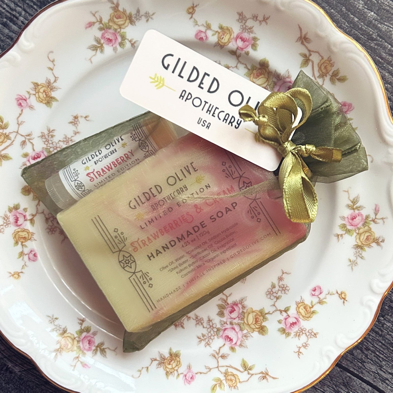 Strawberries & Cream Soap & Lip Balm in a green gift bag on a vintage dish